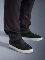 Alpinestars Flex-AST Cargo Pants, negros, pantalones de moto urbanos, primer plano de las piernas ahusadas y dobladillos elásticos, combinados con zapatillas blancas y negras, tejido técnico de sarga de policotton para conducción casual en carretera