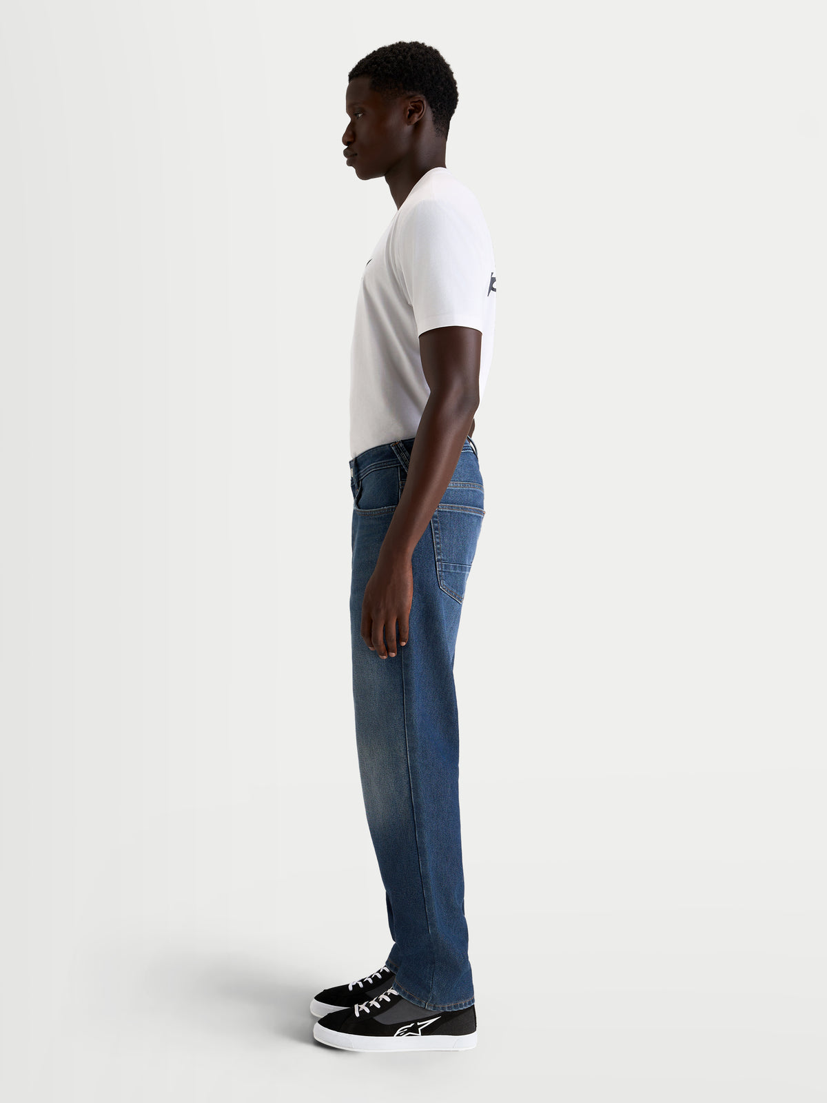 Alpinestars Flex Ast 8 Denim Pantalones, pantalones de moto urbanos para hombre, azul medio, vista de perfil lateral en modelo con camiseta blanca y zapatos de moto, denim monocapa elástico con certificación AA