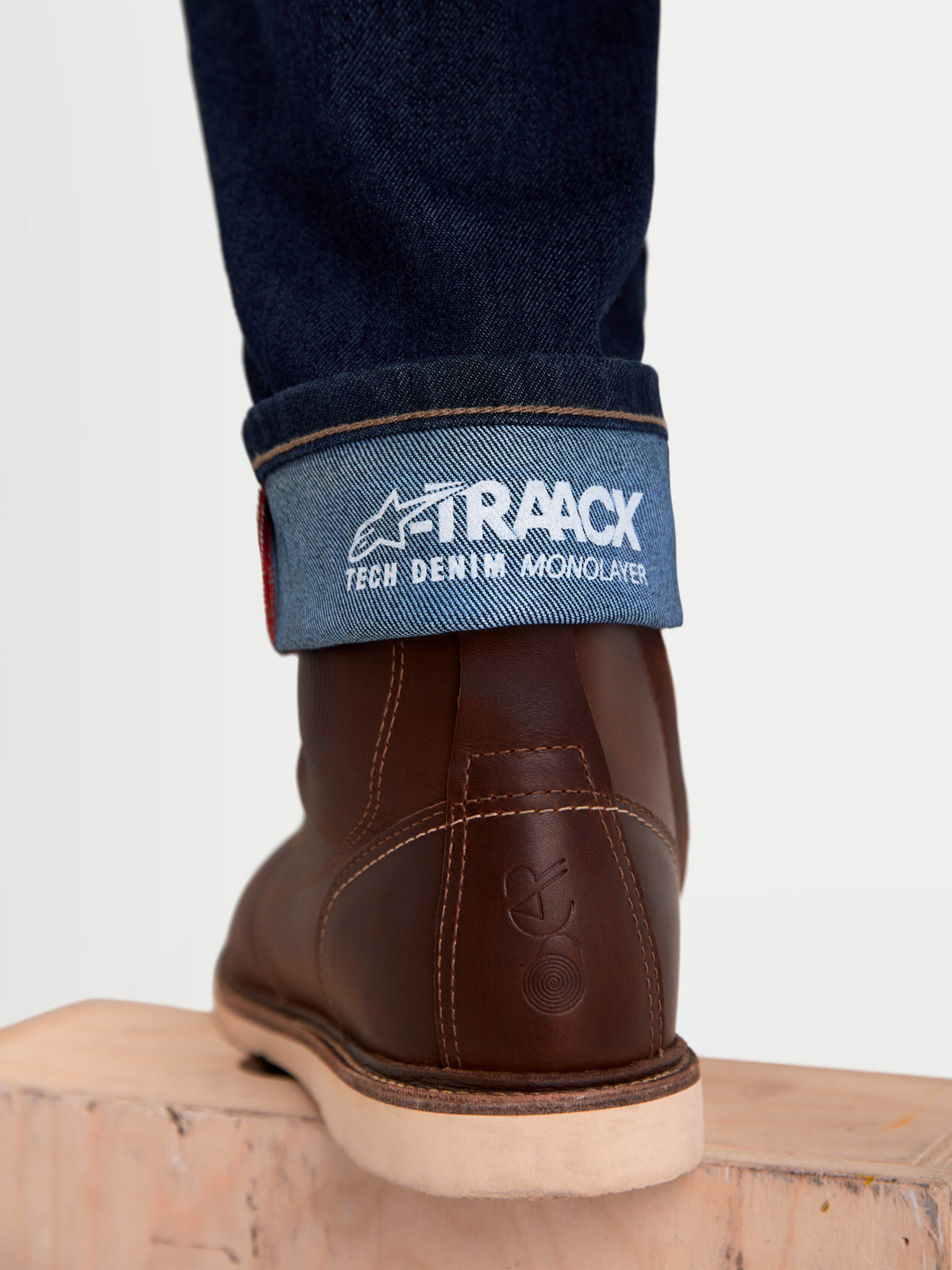 Alpinestars Flex-AST 7 Denim Pants, men's urban motorcycle riding jeans, dark blue, close-up view of the cuffed hem showing the A-TRAACX technical denim branding and brown leather boots
