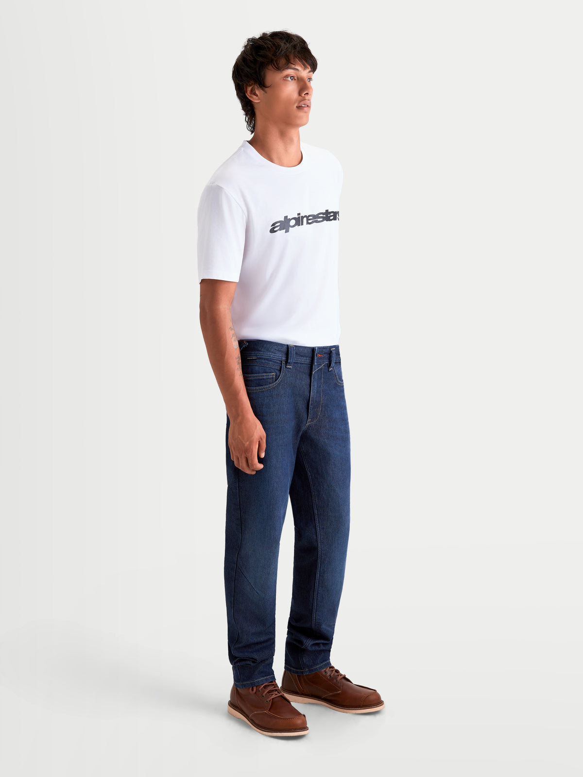 Alpinestars Flex-AST 7 Denim Pants, men's urban contemporary motorcycle jeans in dark blue, side profile view on a model wearing a white t-shirt and brown boots, AA-rated single-layer riding apparel with stretch comfort