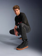 Pantalones Alpinestars C-1 Air, pantalones de moto urbanos, negros, modelo agachado en un estudio, combinados con una camiseta negra de manga larga y zapatillas negras con suela color canela, con paneles de malla transpirable y un estilo urbano contemporáneo