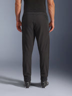 Pantalones Alpinestars Aeroshell Airflow, negros, vista trasera, con zonas perforadas por láser en las pantorrillas y paneles de malla, usados con botas Alpinestars negras, diseño de softshell ligero para deporte y turismo