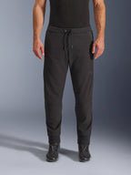 Pantalones Alpinestars Aeroshell Airflow, pantalones de moto negros, vista frontal con botas de conducción negras, cuentan con cintura con cordón y puños de tobillo entallados, diseño de softshell ligero con marca tonal sutil.