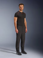 Pantalones Alpinestars Aeroshell Airflow, pantalones de motociclismo negros, toma de estudio de cuerpo completo de un modelo con pantalones softshell de cintura con cordón y puños elásticos, combinados con una camiseta de capa base Alpinestars negra y calzado de conducción negro.