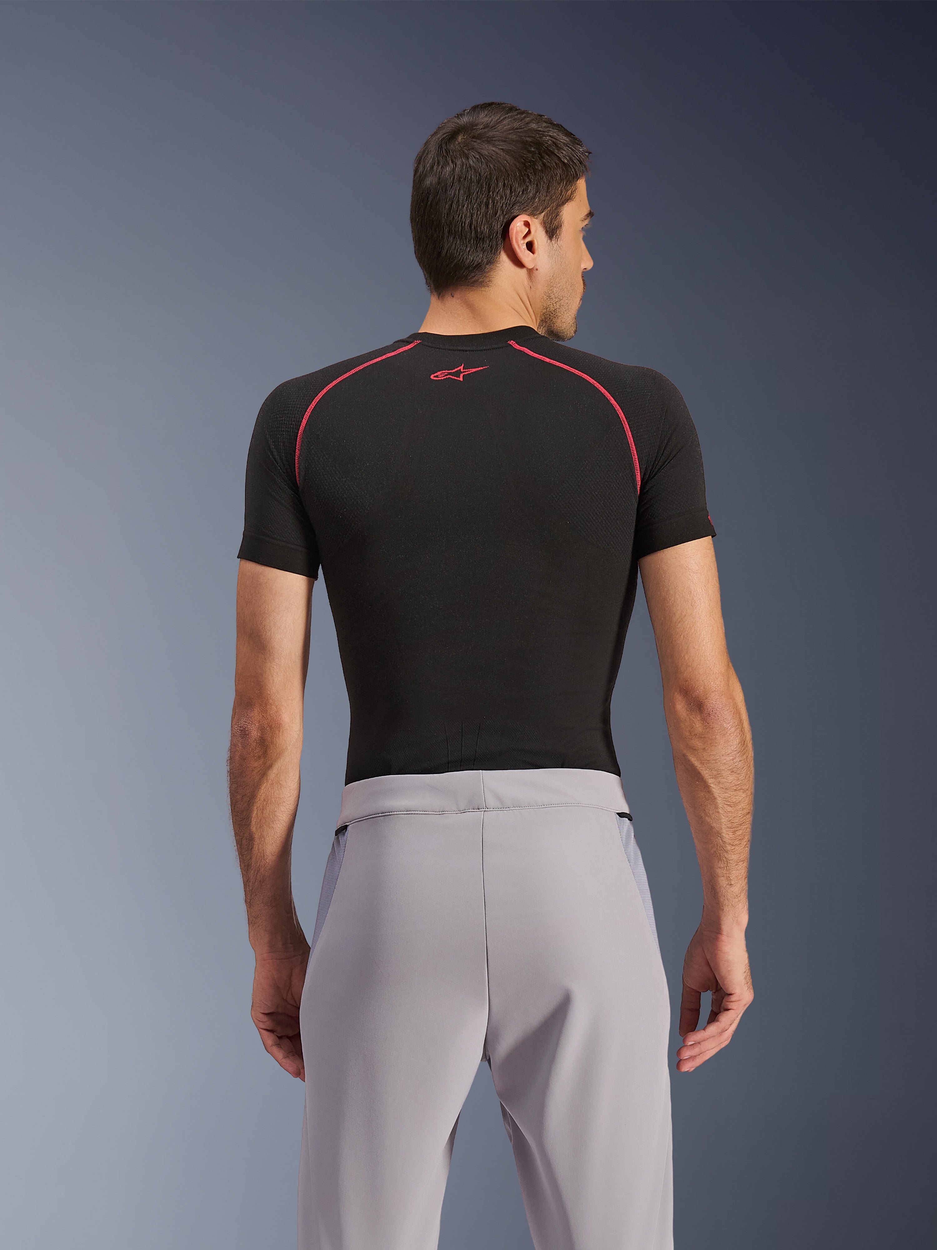 Pantalones Alpinestars Aeroshell Airflow, Gris Medio, vista trasera, combinados con una capa base de manga corta negra con costuras y logotipo rojos, con tejido softshell elástico ligero y paneles de malla para una ventilación máxima, ajuste deportivo ergonómico para la conducción de motocicletas