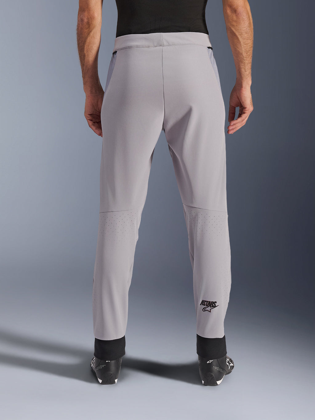 Pantalones Alpinestars Aeroshell Airflow, pantalones de moto, Mid Gray, vista trasera que muestra las zonas perforadas con láser en las pantorrillas y el logotipo negro de Astars, confección en softshell textil con puños negros en los tobillos y paneles de malla en la cadera.