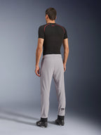 Vista posterior de un modelo con los pantalones Alpinestars Aeroshell Airflow en color Mid Gray, combinados con una camiseta técnica negra y calzado negro, destacando las zonas perforadas con láser en las pantorrillas y el ajuste deportivo atlético.