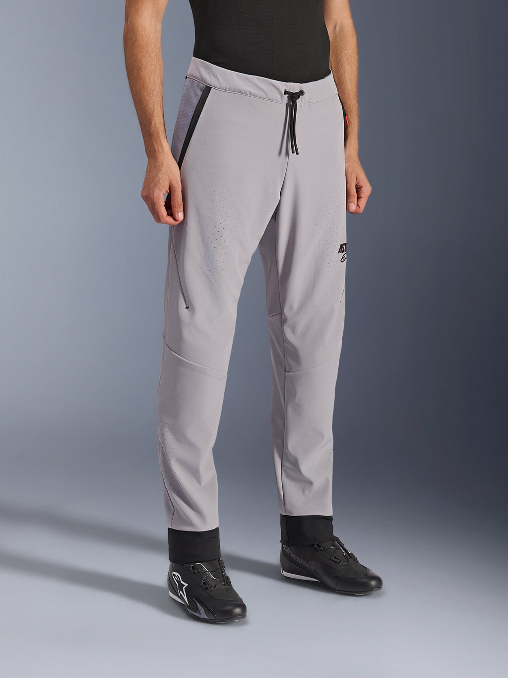 Pantalones Alpinestars Aeroshell Airflow, Gris Medio, pantalones de moto ligeros con zonas de ventilación perforadas con láser en los muslos y las espinillas, cuentan con una cintura elástica con cordón y un ajuste deportivo entallado, mostrados en un modelo con calzado de moto negro.