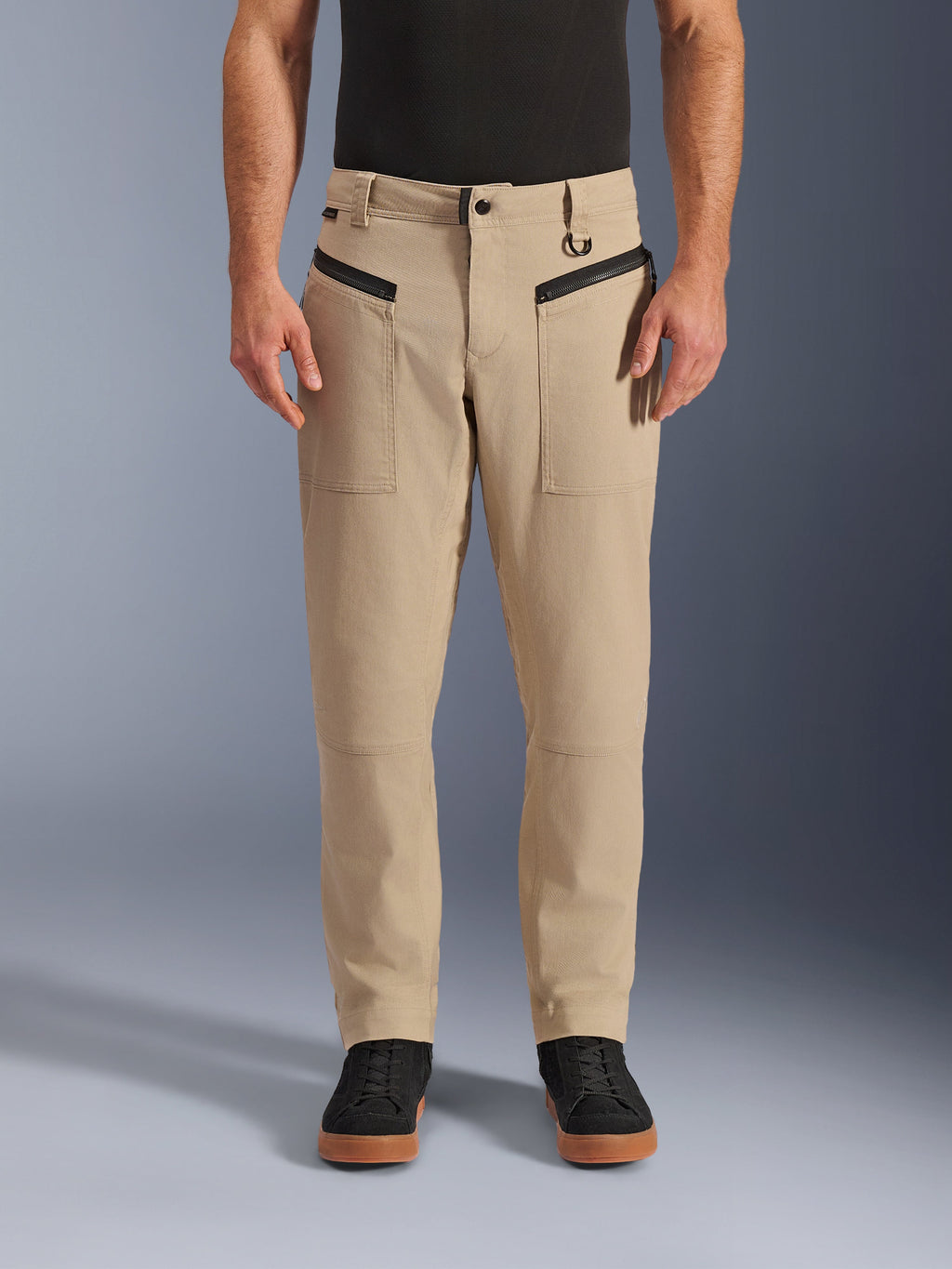 Alpinestars Flex-AST Canvas Pants, pantalones urbanos de moto, color marrón, estilo de ropa de trabajo clásica, con bolsillos frontales con cremallera horizontal negra y anilla en D en la trabilla, combinados con camiseta y zapatos negros, vista frontal de estudio
