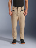 Alpinestars Flex-AST Canvas Pants, pantalones urbanos de moto, color marrón, estilo de ropa de trabajo clásica, con bolsillos frontales con cremallera horizontal negra y anilla en D en la trabilla, combinados con camiseta y zapatos negros, vista frontal de estudio