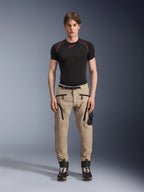 Male model wearing Alpinestars Acteon Pants in Sand, paired with a black short-sleeve base layer and black technical boots, featuring cargo pockets with black zippers and a tapered fit, contemporary urban motorcycle gear