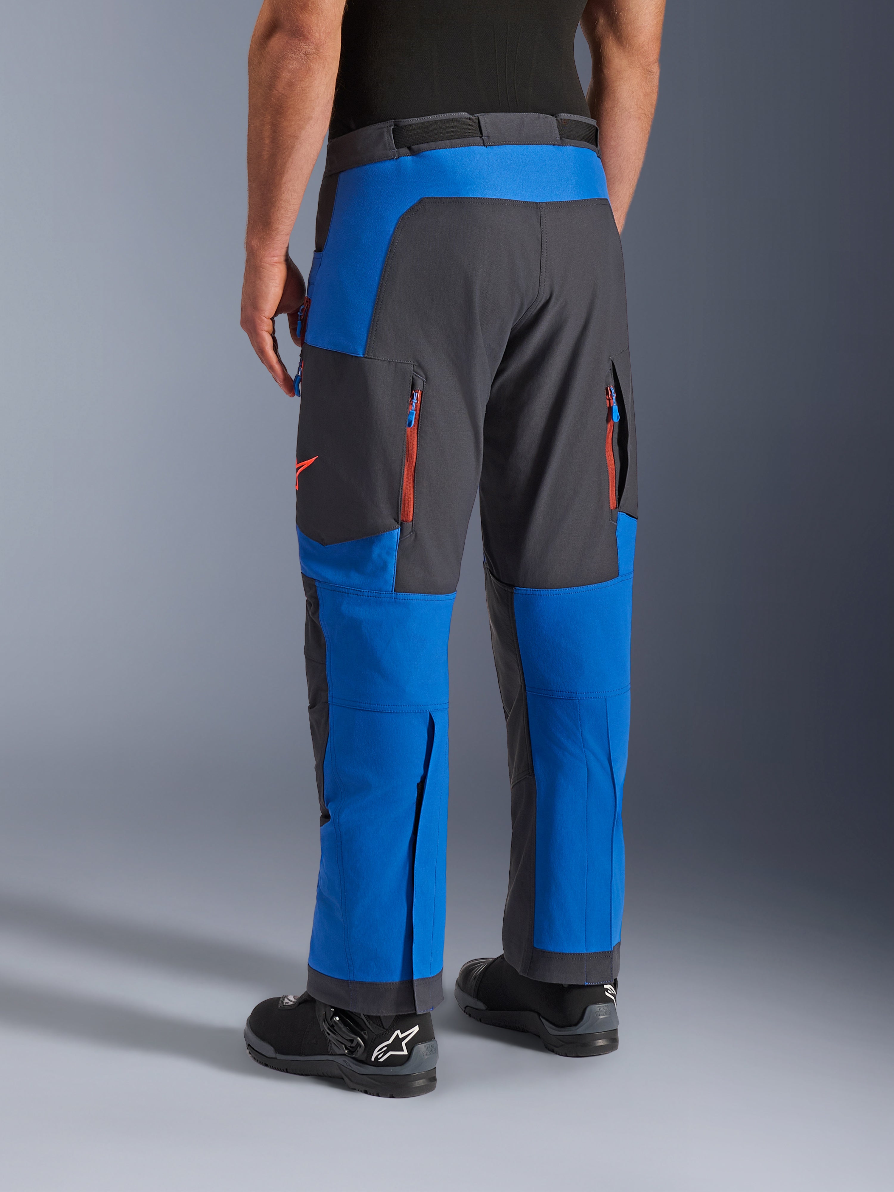 Alpinestars Maxdura Dual Pants, azul real y gris oscuro, vista trasera que muestra bolsillos con cremallera y zonas de ventilación, diseño sobre la bota usado con botas Alpinestars negras, equipamiento duradero para conducción de aventura y dual-sport