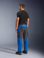 Pantalones Alpinestars Maxdura Dual, pantalones de moto de aventura, azul real y gris oscuro, vista trasera lateral usados por un modelo, con ventilaciones de cremallera naranja, ajuste sobre la bota y material elástico duradero