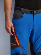 Pantalones Alpinestars Maxdura Dual en azul real y gris oscuro, vista de primer plano de la cintura con hebilla magnética, bolsillo cargo con cremallera y detalles en naranja y logotipo rojo de Alpinestars, equipamiento técnico para motociclismo de aventura
