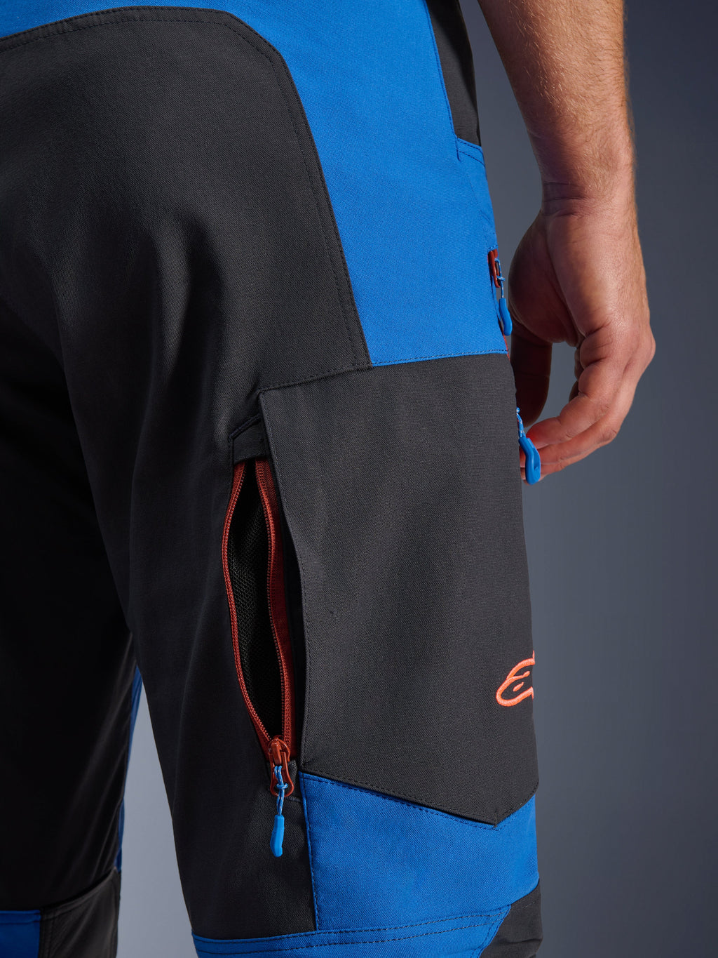 Alpinestars Maxdura Dual Pants, azul real y gris oscuro, primer plano del bolsillo de carga lateral con cremallera, tiradores de cremallera azules, logotipo bordado en naranja, equipamiento para conducción de motocicletas de aventura
