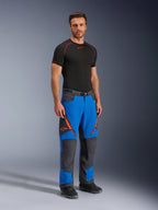 Pantalones Alpinestars Maxdura Dual, pantalones de motociclismo de aventura, azul real y gris oscuro, con detalles de cremalleras y logotipos en naranja, usados por un modelo con una capa base negra y botas, diseño técnico con paneles reforzados para conducción dual-sport