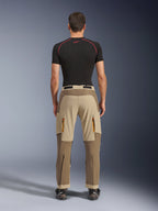 Pantalones Alpinestars Maxdura Dual en Walnut Aluminum, vista trasera que muestra un diseño bitono en marrón y tostado, pantalones para conducción de aventura con bolsillos de carga con cremallera y asiento reforzado, usados con una camiseta de compresión negra y botas de motociclismo.