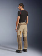 Pantalones Alpinestars Maxdura Dual, pantalones de conducción Adventure y Dual-Sport, Walnut Aluminum, vista trasera usados por un modelo con una capa base negra y botas de moto, con construcción de paneles múltiples, ventilaciones traseras con cremallera y refuerzos superpuestos.