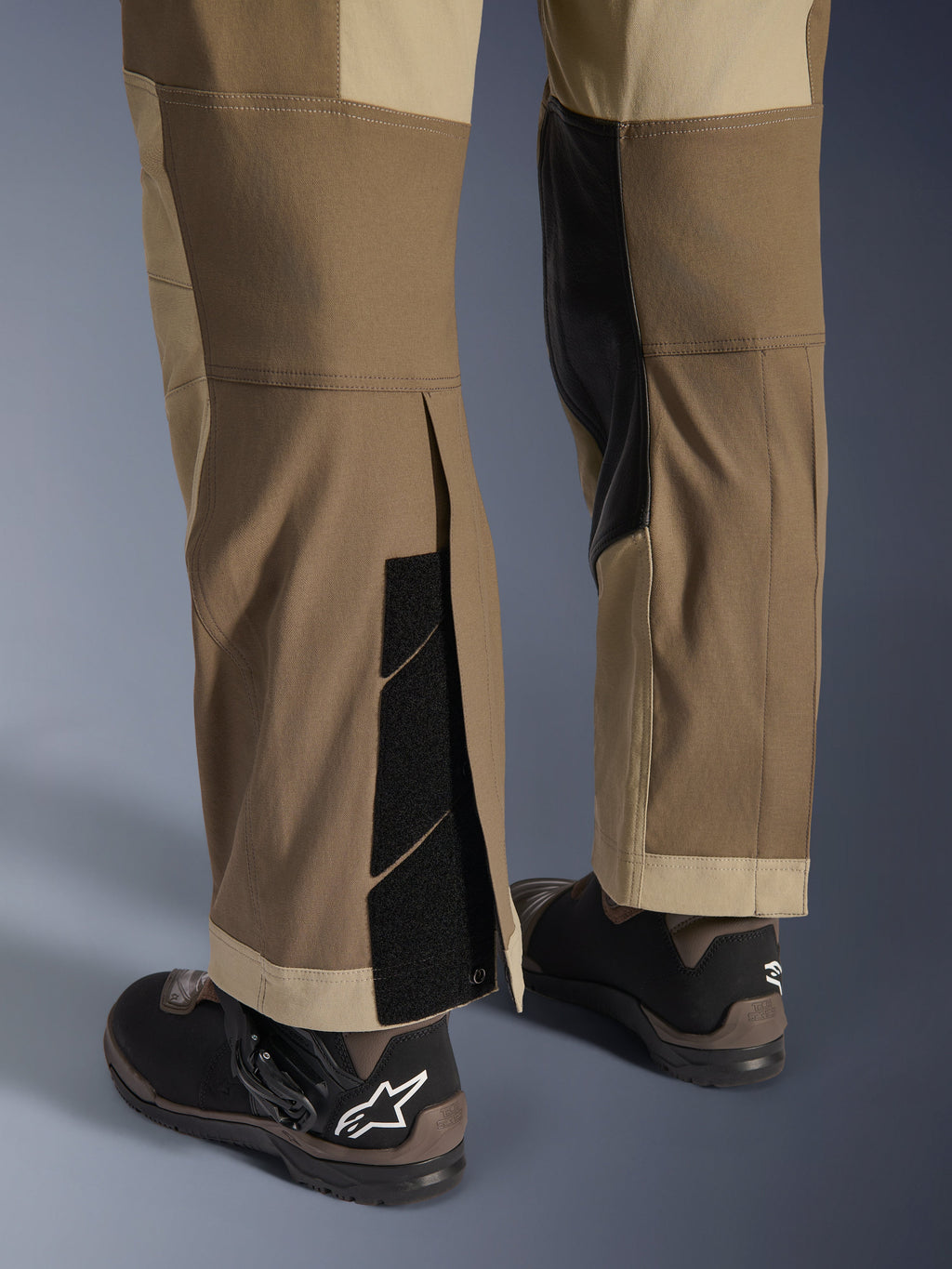 Pantalones Alpinestars Maxdura Dual en Walnut Aluminum, vista detallada de la parte inferior de la pierna y el dobladillo con diseño sobre la bota, cierres de velcro ajustables y paneles interiores reforzados, combinados con botas de moto negras.
