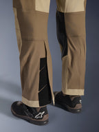 Pantalones Alpinestars Maxdura Dual en Walnut Aluminum, vista detallada de la parte inferior de la pierna y el dobladillo con diseño sobre la bota, cierres de velcro ajustables y paneles interiores reforzados, combinados con botas de moto negras.