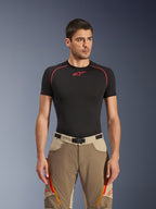 Alpinestars Maxdura Dual Pants en Walnut Aluminum, pantalones de motociclismo de aventura en tonos canela y beige usados por un modelo con una camiseta de capa base negra, con ventilaciones en los muslos con cremallera naranja, logotipos rojos y una hebilla magnética en la cintura, retrato de estudio.