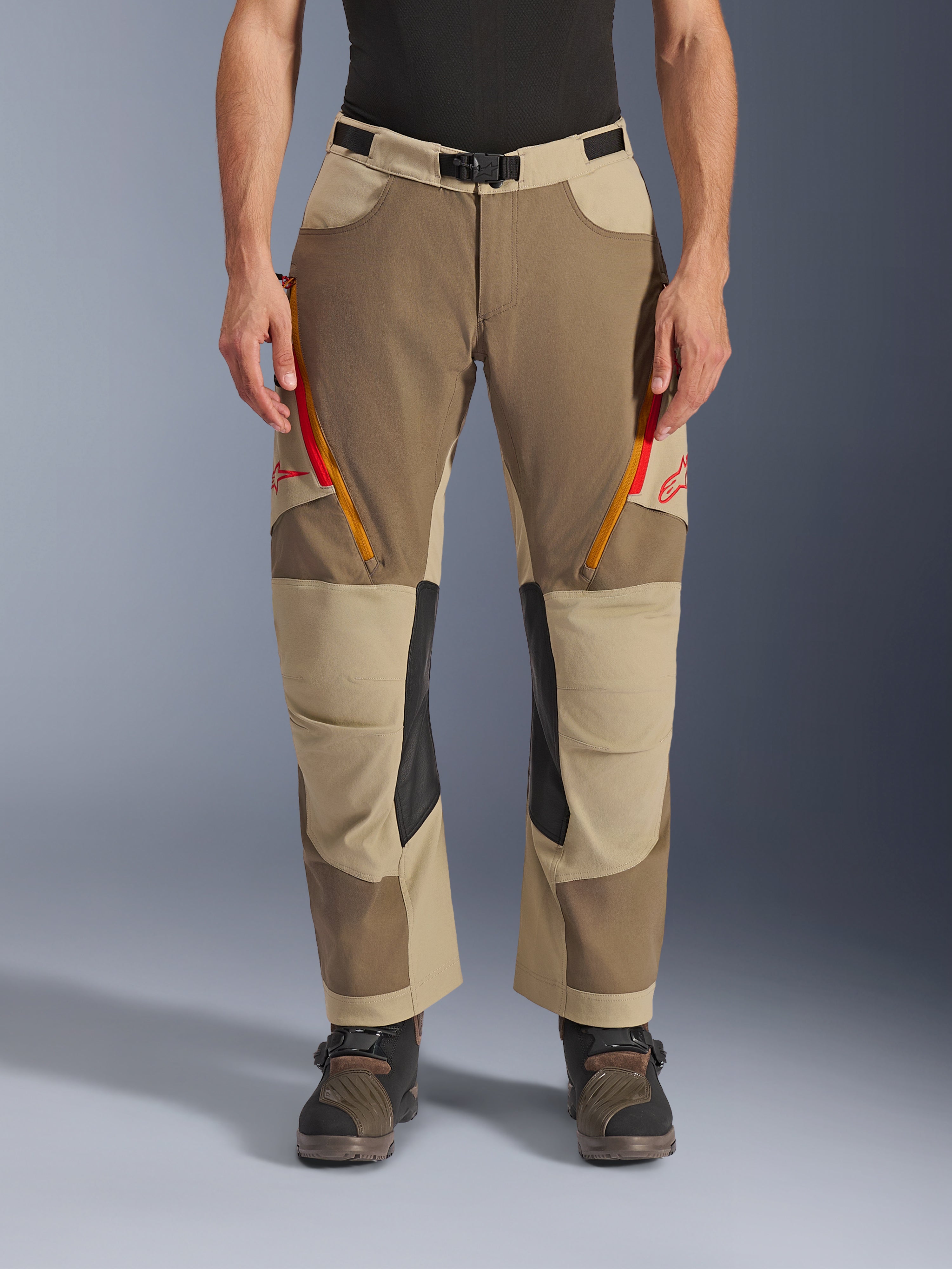 Pantalones Alpinestars Maxdura Dual, Walnut Aluminum, pantalones de moto de aventura con ventilaciones en los muslos con cremalleras rojas y naranjas, paneles interiores de cuero negro en las rodillas, usados con una capa base negra y botas robustas, diseño multitonal duradero para conducción dual-sport