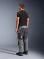 Pantalones Alpinestars Maxdura Dual, pantalones de aventura para motociclismo, gris oscuro y gris intenso, usados por un modelo en una vista lateral trasera, con detalles rojos en las cremalleras y el logotipo, paneles grises reforzados, bolsillos tipo cargo y ajuste sobre la bota