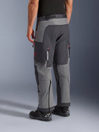 Pantalones Alpinestars Maxdura Dual, pantalones de moto de aventura, gris oscuro y gris intenso, vista trasera con construcción de múltiples paneles, detalles de cremalleras rojas y logo de estrella, combinados con botas Alpinestars negras, diseñados para rendimiento dual-sport