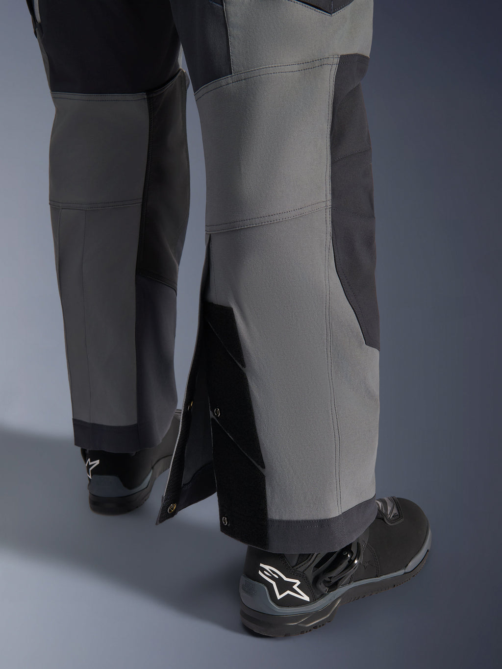 Pantalones Alpinestars Maxdura Dual, pantalones de motociclismo de aventura, gris oscuro y gris intenso, vista de cerca del dobladillo ajustable sobre la bota con cierres a presión y paneles reforzados, usados con botas Alpinestars negras, diseño técnico robusto para conducción dual-sport