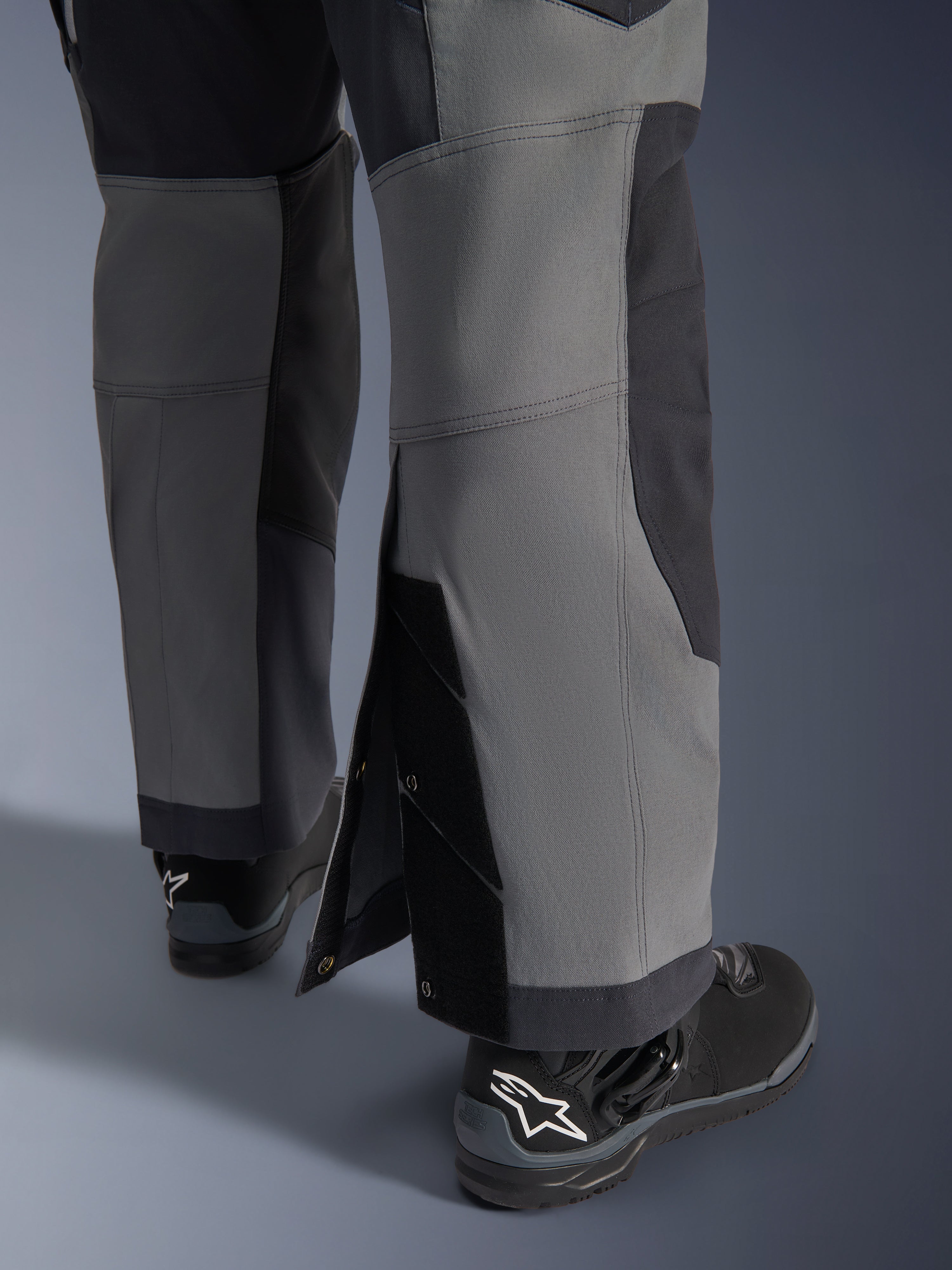 Pantalones Alpinestars Maxdura Dual, pantalones de motociclismo de aventura, gris oscuro y gris intenso, vista de cerca del dobladillo ajustable sobre la bota con cierres a presión y paneles reforzados, usados con botas Alpinestars negras, diseño técnico robusto para conducción dual-sport
