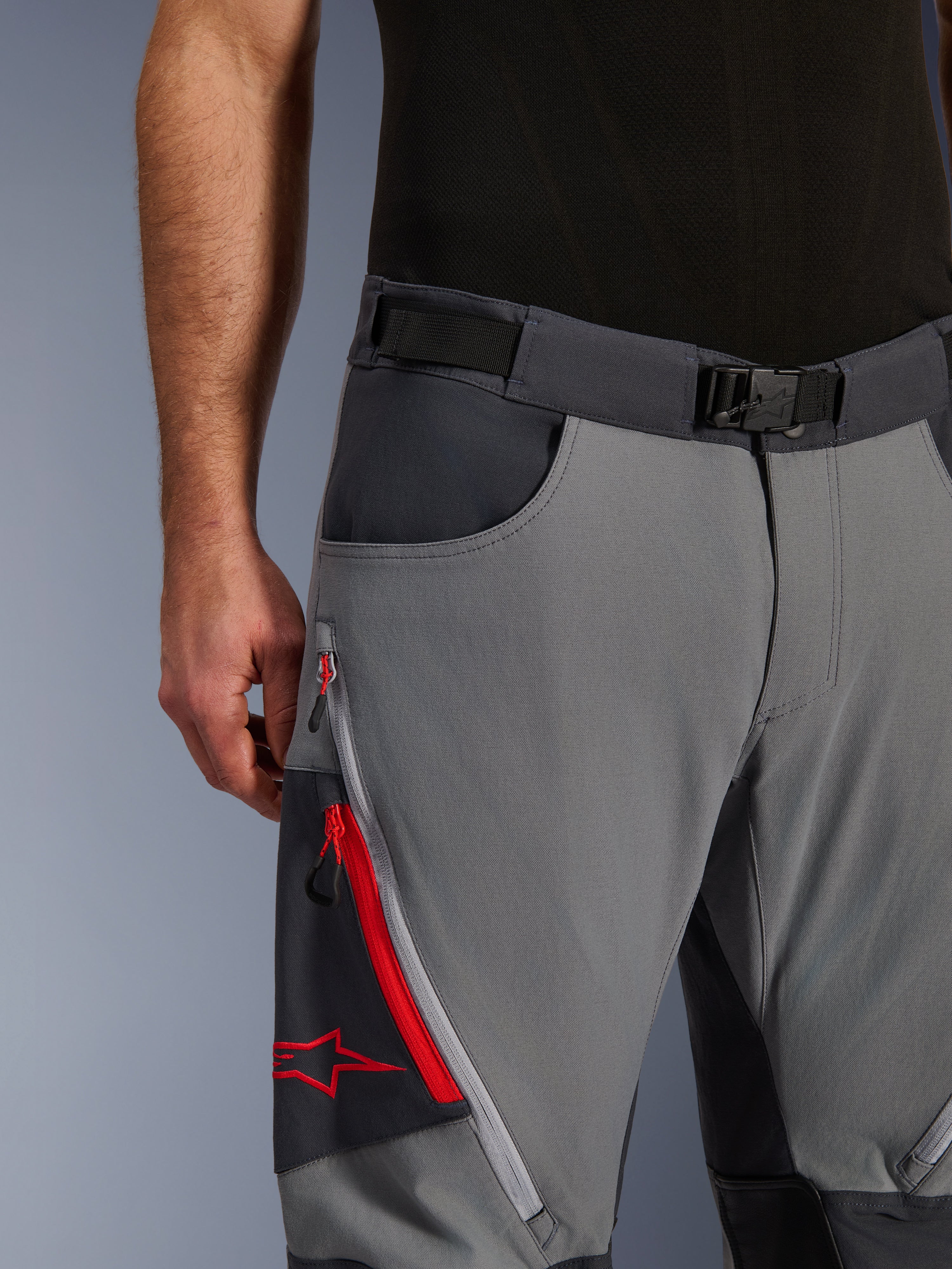 Pantalones Alpinestars Maxdura Dual, pantalones de motociclismo de aventura, gris oscuro y gris intenso, primer plano con cinturón ajustable con hebilla magnética, bolsillo de carga con cremallera con detalles rojos y logotipo de Alpinestars