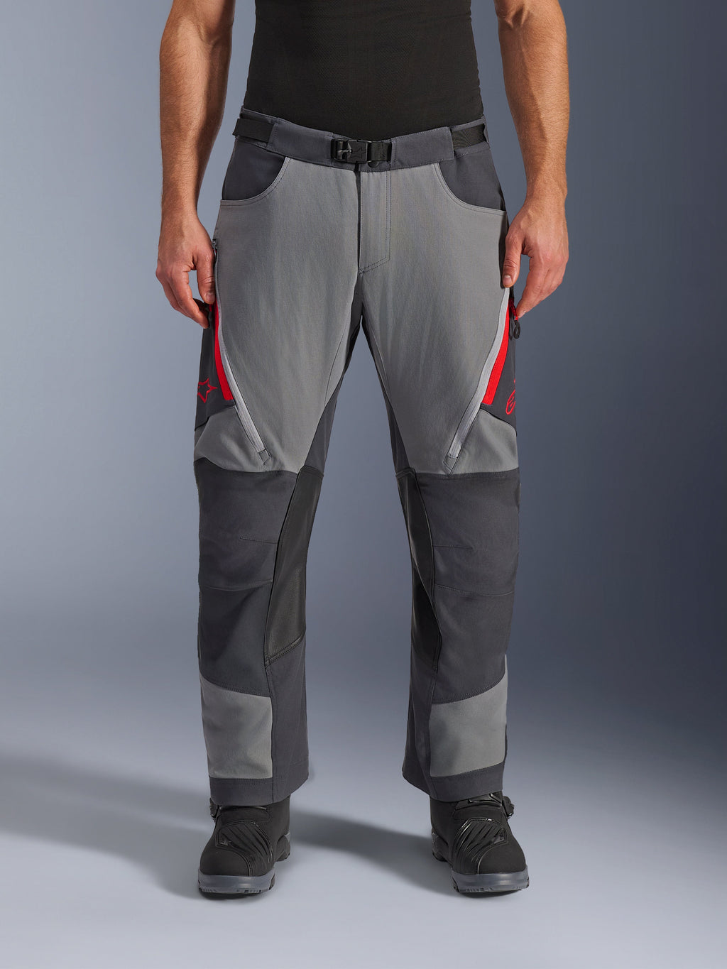 Alpinestars Maxdura Dual Pants, pantalones de aventura para moto, gris oscuro y gris intenso con detalles rojos, vista frontal que muestra ventilaciones con cremallera en los muslos, cinturón con hebilla magnética y paneles reforzados en las rodillas, diseño sobre la bota para conducción dual-sport.