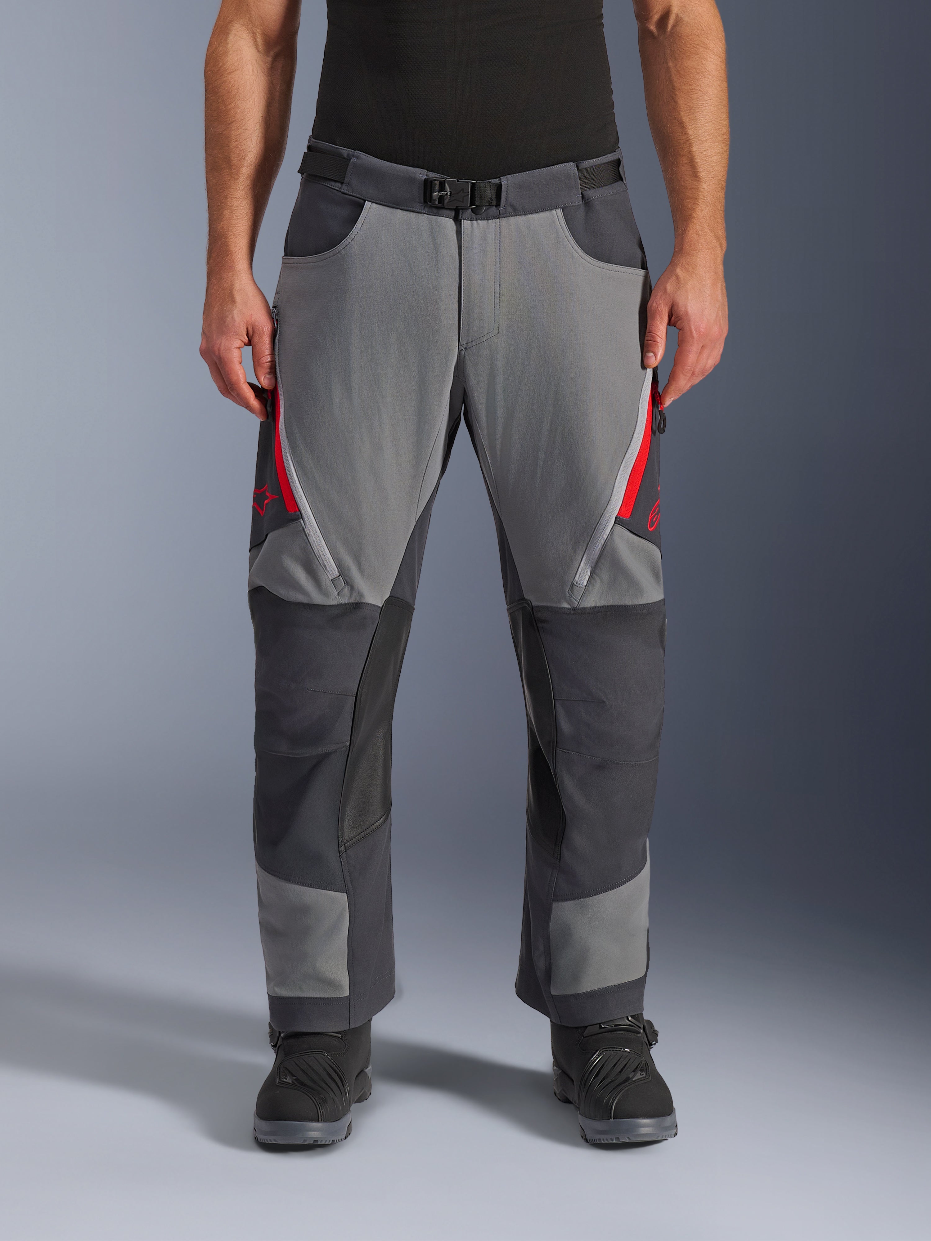Alpinestars Maxdura Dual Pants, pantalones de aventura para moto, gris oscuro y gris intenso con detalles rojos, vista frontal que muestra ventilaciones con cremallera en los muslos, cinturón con hebilla magnética y paneles reforzados en las rodillas, diseño sobre la bota para conducción dual-sport.