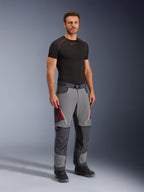Pantalones Alpinestars Maxdura Dual, pantalones de moto de aventura, gris oscuro y gris intenso, usados con una capa base negra y botas, con aberturas de ventilación rojas con cremallera, paneles reforzados en las rodillas y el asiento, y cintura con cinturón, ajuste atlético para conducción dual-sport