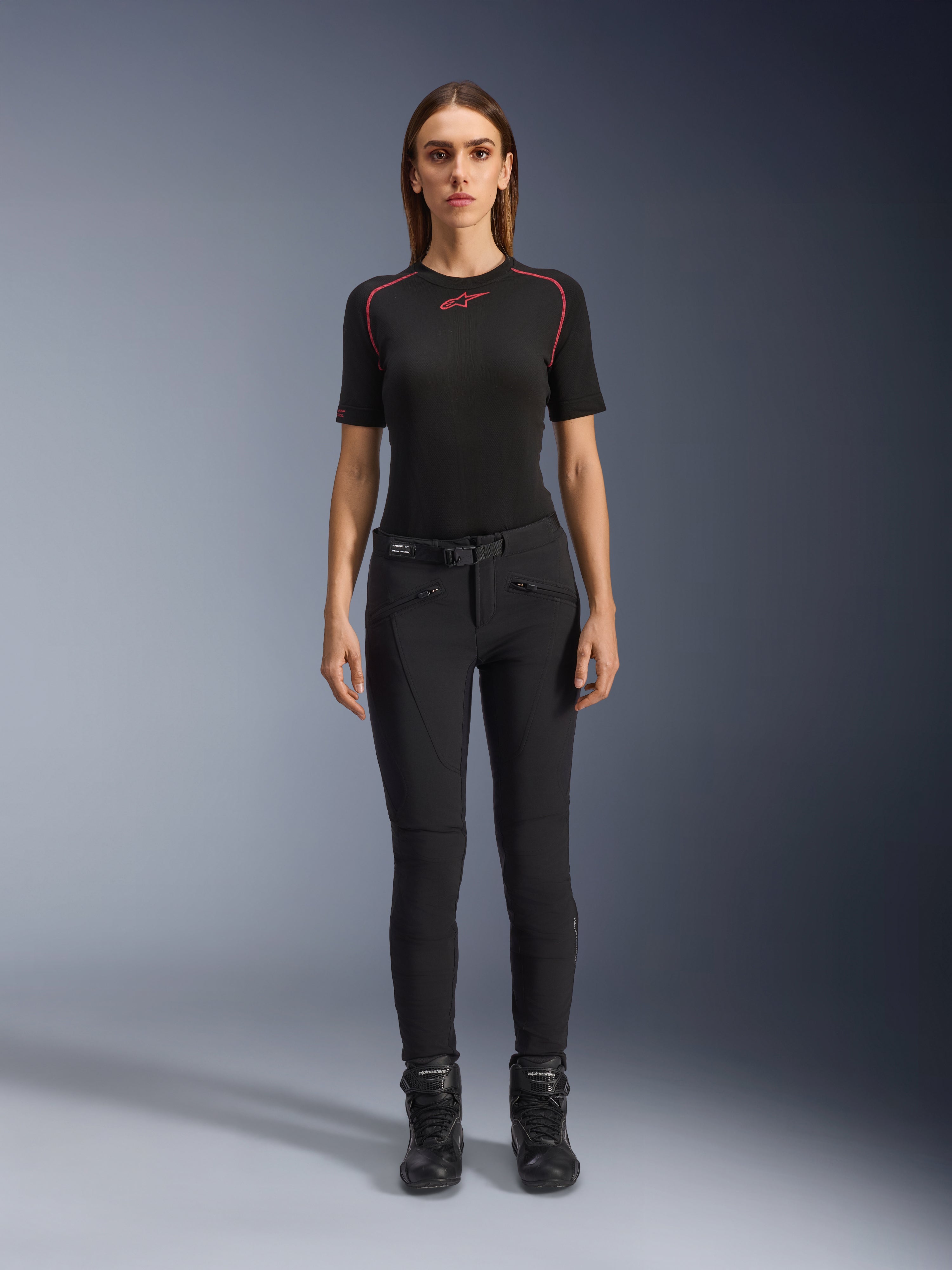 Pantalones Alpinestars Alamosa para mujer, pantalones de moto negros de ajuste ceñido, mostrados en una modelo de frente, con bolsillos delanteros con cremallera y cinturón integrado, estilo minimalista inspirado en el streetwear para conducción urbana