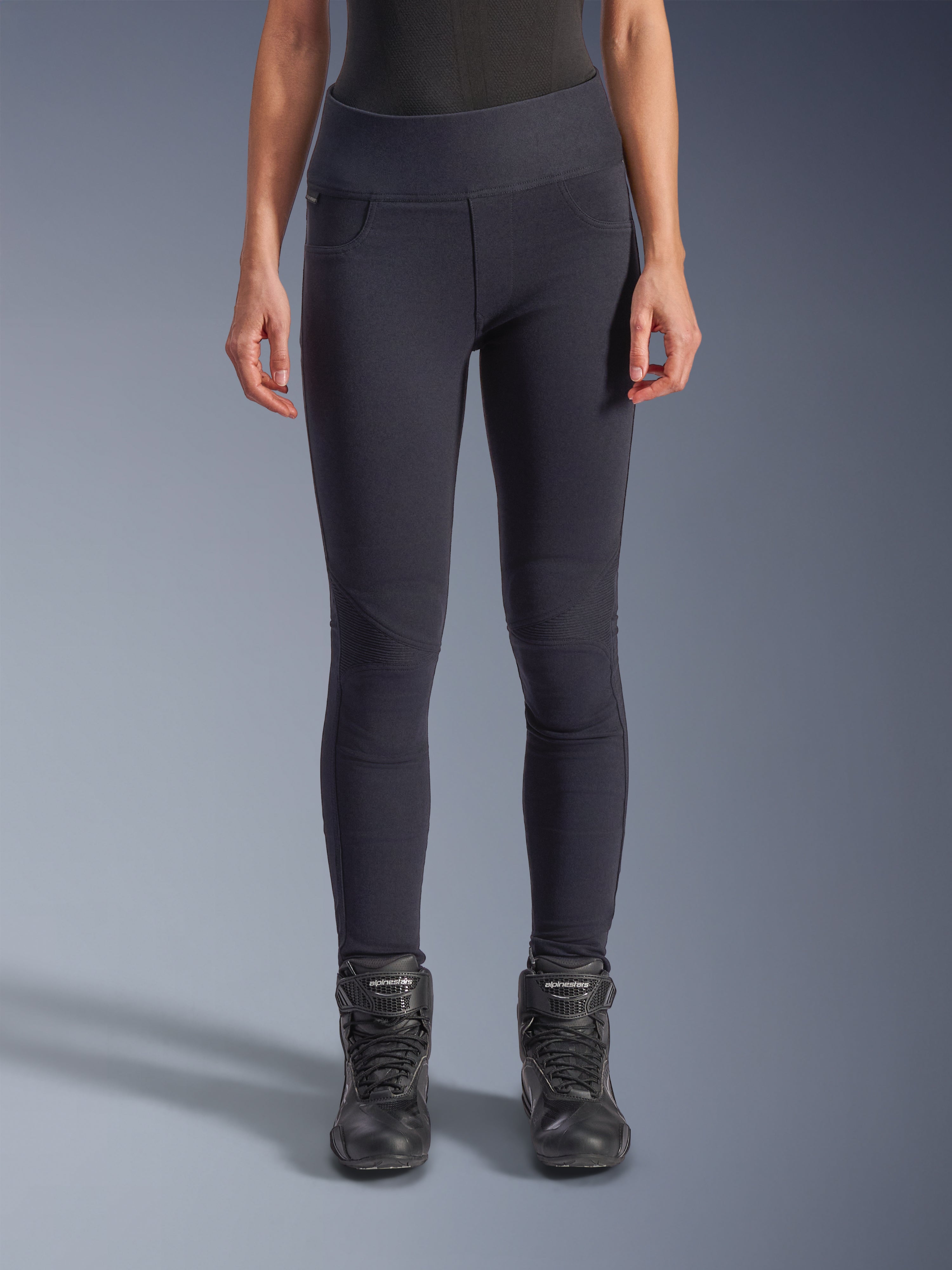Alpinestars Stella Flex-Ast Leggings, leggings de moto para mujer, negro, ajuste de cintura alta con paneles articulados en las rodillas y costuras contorneadas, lucidos por una modelo con botas de moto negras, ropa de moto de alto rendimiento urbano