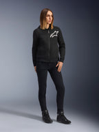 Mujer con Alpinestars Daisy V3 Women's Riding Denim, pantalones de moto para mujer en color Rinse Black, corte ajustado, combinados con sudadera negra con capucha y botas de moto, equipamiento de protección urbano casual