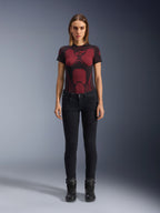Alpinestars Daisy V3 Women's Riding Denim, pantalones de moto para mujer de corte ajustado en color Rinse Black, lucidos por una modelo con una camiseta técnica de patrón rojo y negro y botas de moto negras, equipamiento de conducción urbana casual con silueta femenina y diseño de talle alto.