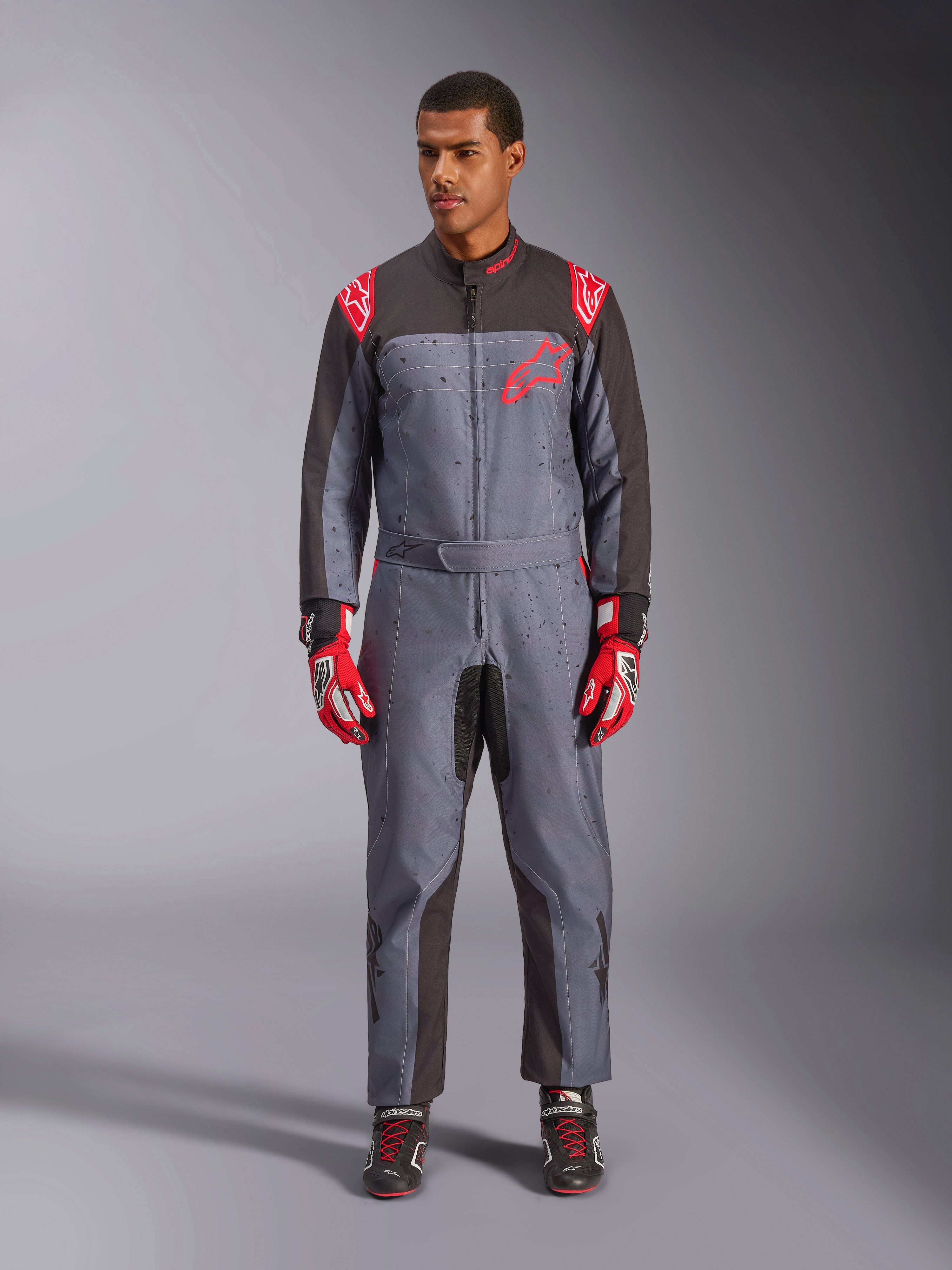 Mono Alpinestars KMX-9 V3 Graphic 6, mono de karting, negro antracita y rojo, patrón gráfico con motas grises, paneles negros en la parte interna de brazos y piernas, logotipos Alpinestars rojos en hombros y pecho, usado con guantes de carreras rojos y calzado negro