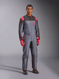 Mono de karting Alpinestars KMX-9 V3 Graphic 6, gris y antracita con acentos rojos, con un gráfico de salpicaduras único en el pecho y las piernas, combinado con guantes de carreras rojos y botas de karting negras, fotografía de estudio de cuerpo completo.