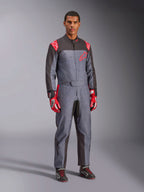 Mono de karting Alpinestars KMX-9 V3 Graphic 6, gris y antracita con acentos rojos, con un gráfico de salpicaduras único en el pecho y las piernas, combinado con guantes de carreras rojos y botas de karting negras, fotografía de estudio de cuerpo completo.