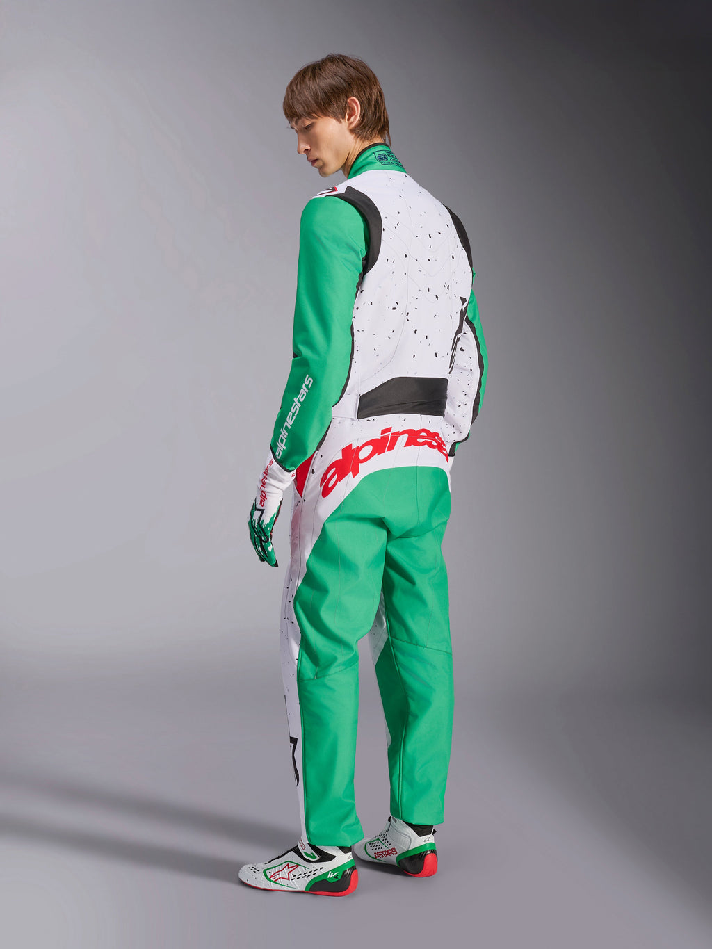 Alpinestars KMX-9 V3 Graphic 6, mono de karting, blanco, verde y rojo, modelo visto desde la parte posterior, con mangas y paneles inferiores verdes, parte superior del torso blanca con detalles de motas negras, llamativo logotipo de Alpinestars en rojo en la zona lumbar, combinado con calzado de karting a juego en blanco y verde