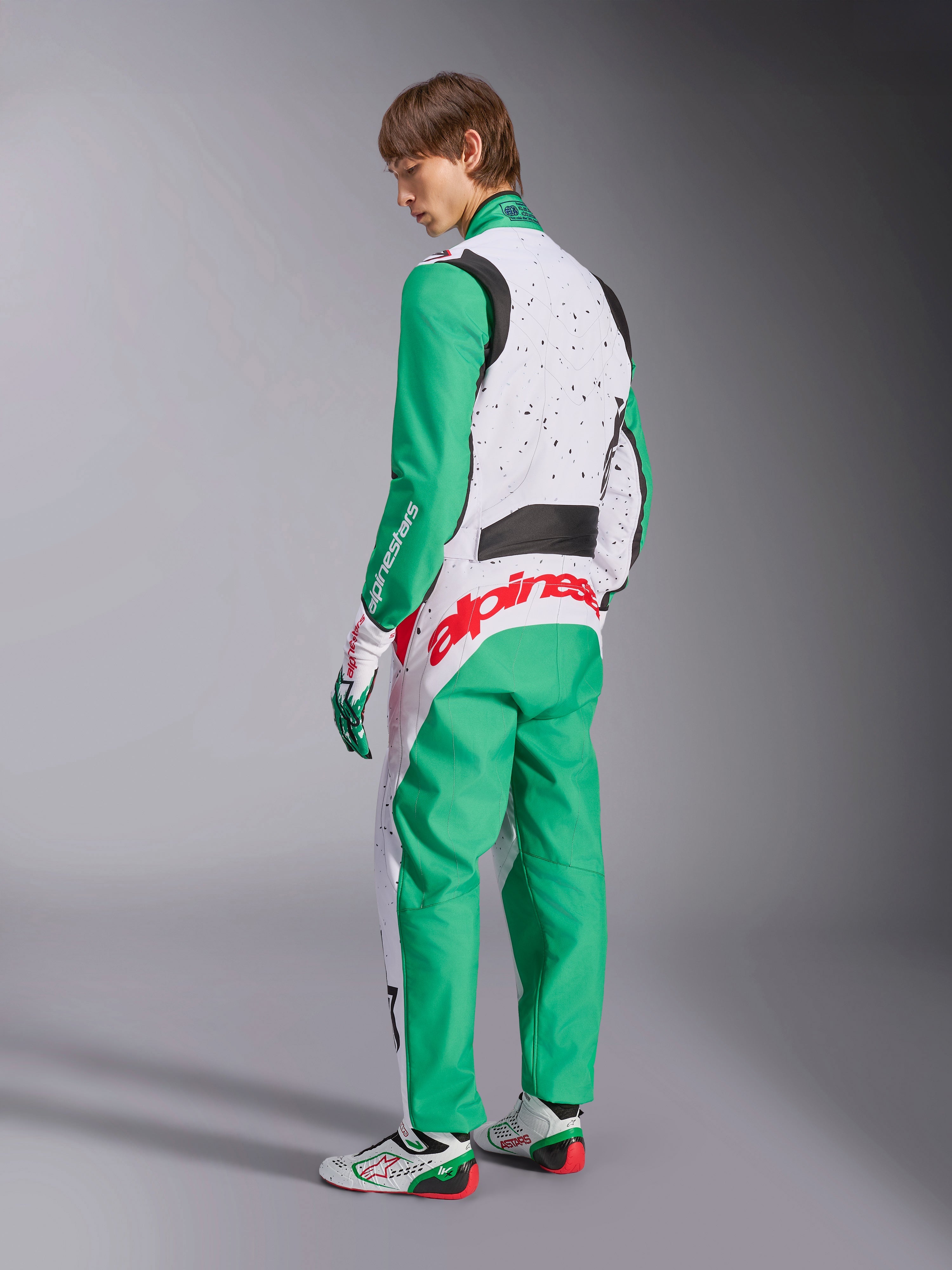 Alpinestars KMX-9 V3 Graphic 6, mono de karting, blanco, verde y rojo, modelo visto desde la parte posterior, con mangas y paneles inferiores verdes, parte superior del torso blanca con detalles de motas negras, llamativo logotipo de Alpinestars en rojo en la zona lumbar, combinado con calzado de karting a juego en blanco y verde