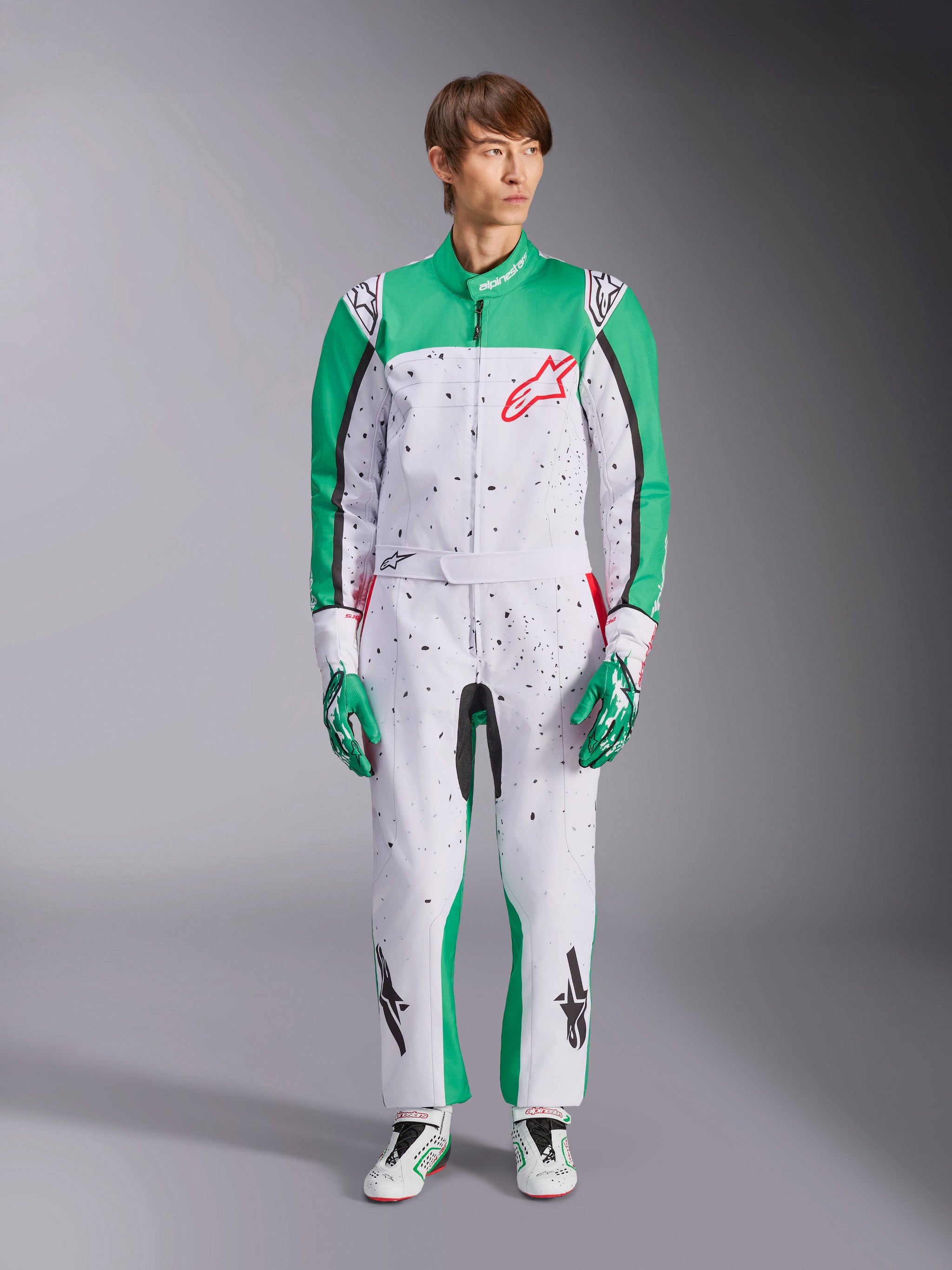 Alpinestars KMX-9 V3 Graphic 6 Suit, blanco, verde y rojo, mono de karting de una pieza con un patrón gráfico de salpicaduras negras, paneles verdes en las mangas y las piernas, logotipo rojo de Alpinestars en el pecho, usado con guantes y calzado de competición a juego