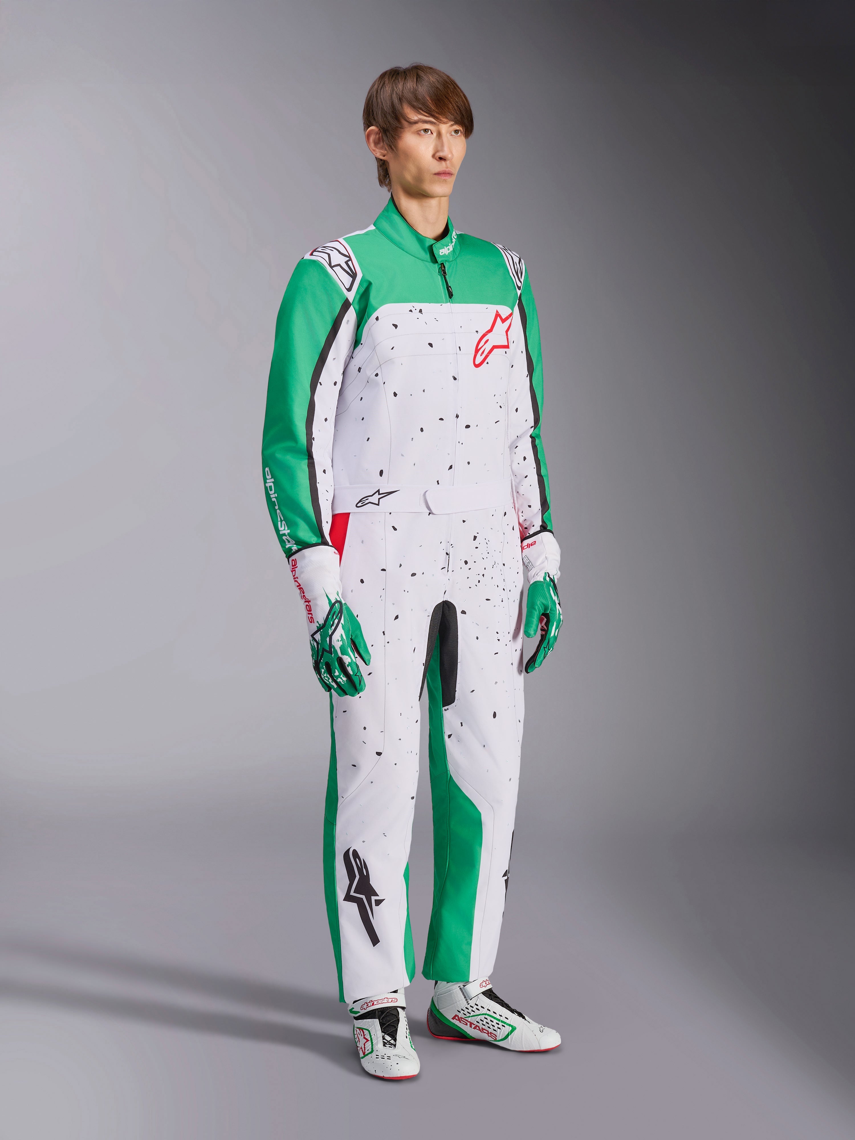 Mono Alpinestars KMX-9 V3 Graphic 6, mono de karting, blanco, verde y rojo, usado con guantes y calzado de competición a juego, cuenta con un cuerpo blanco con mangas verdes y gráficos de salpicaduras negras, logotipo rojo de Alpinestars en el pecho, diseño deportivo de una sola pieza para automovilismo