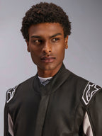 Alpinestars GP Race V3 Suit FIA, mono de automovilismo negro usado por un hombre, vista en primer plano que muestra el cuello suave y los logotipos de estrellas blancas en las hombreras, equipo de protección profesional para automovilismo.