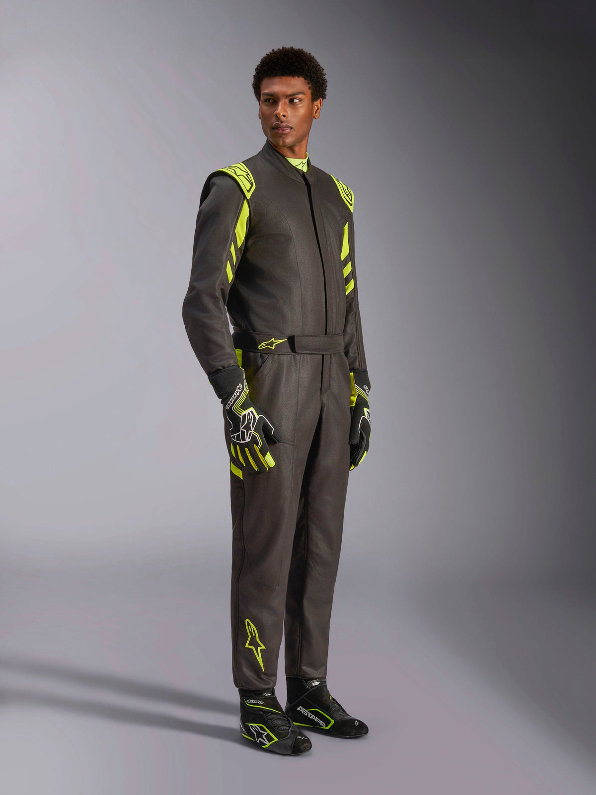 Alpinestars GP Race V3 Suit FIA, mono de automovilismo, negro y amarillo flúor, lucido por un modelo con guantes y botas de carreras a juego, con detalles en amarillo vibrante en los hombros y las piernas, equipamiento profesional de automovilismo