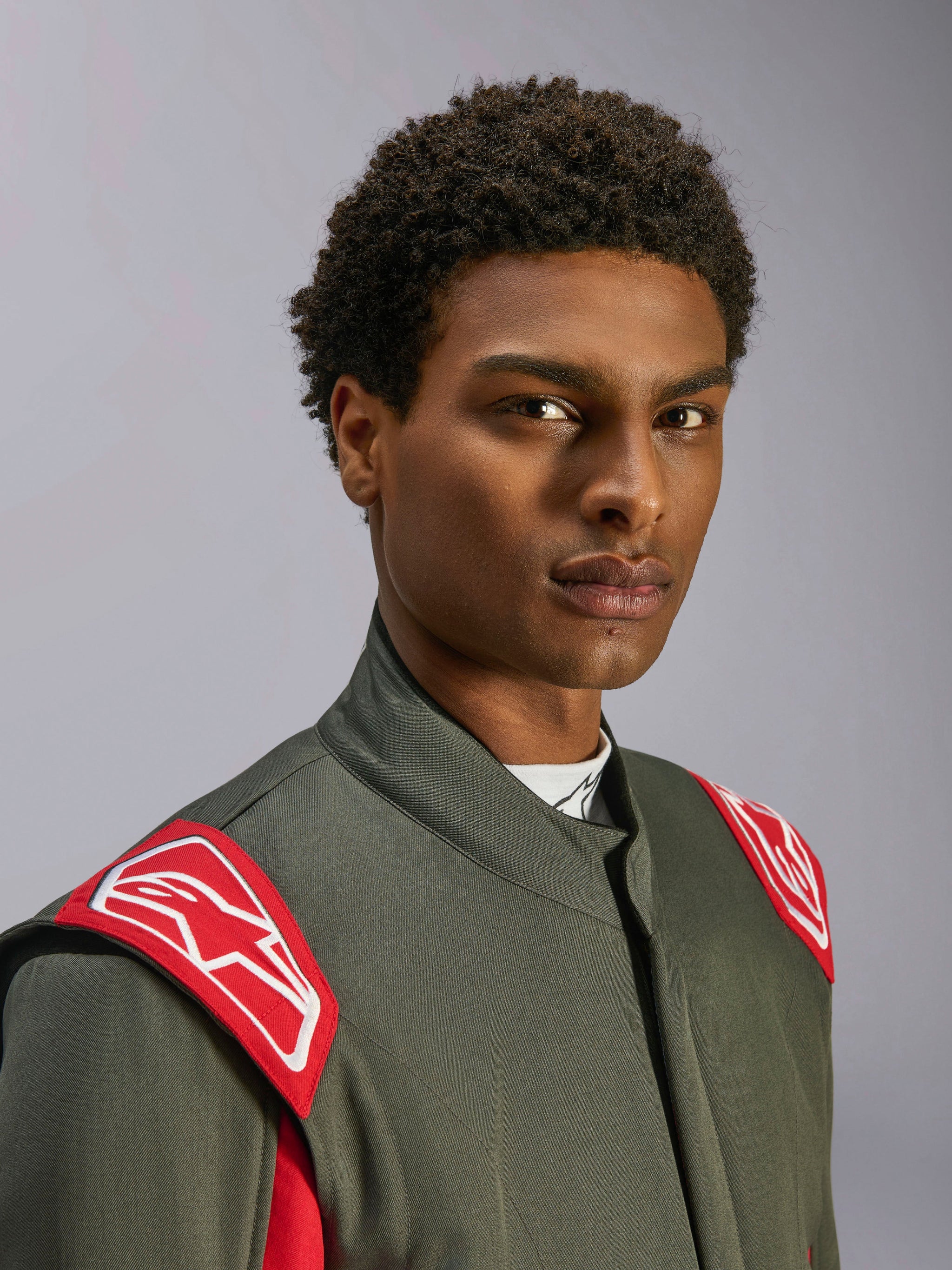 Alpinestars GP Race V3 Suit FIA, Auto Racing Suit, Anthracite Red, close-up of the upper torso and head, featuring red shoulder epaulettes with white Alpinestars logo, high collar and grey twill material