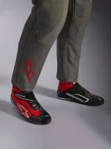 Alpinestars GP Race V3 Suit FIA, Anthracite Red racing suit, close-up of lower legs with embroidered red star logo, paired with red and black racing boots, professional automotive gear designed for driver protection and comfort