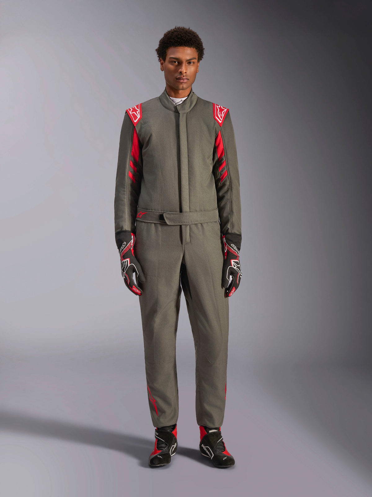 Alpinestars GP Race V3 Suit FIA, mono de automovilismo, color antracita y rojo, usado por un modelo masculino con guantes y botas a juego, con hombreras rojas y logotipos de la marca, equipamiento profesional de automovilismo para conducción de alto rendimiento